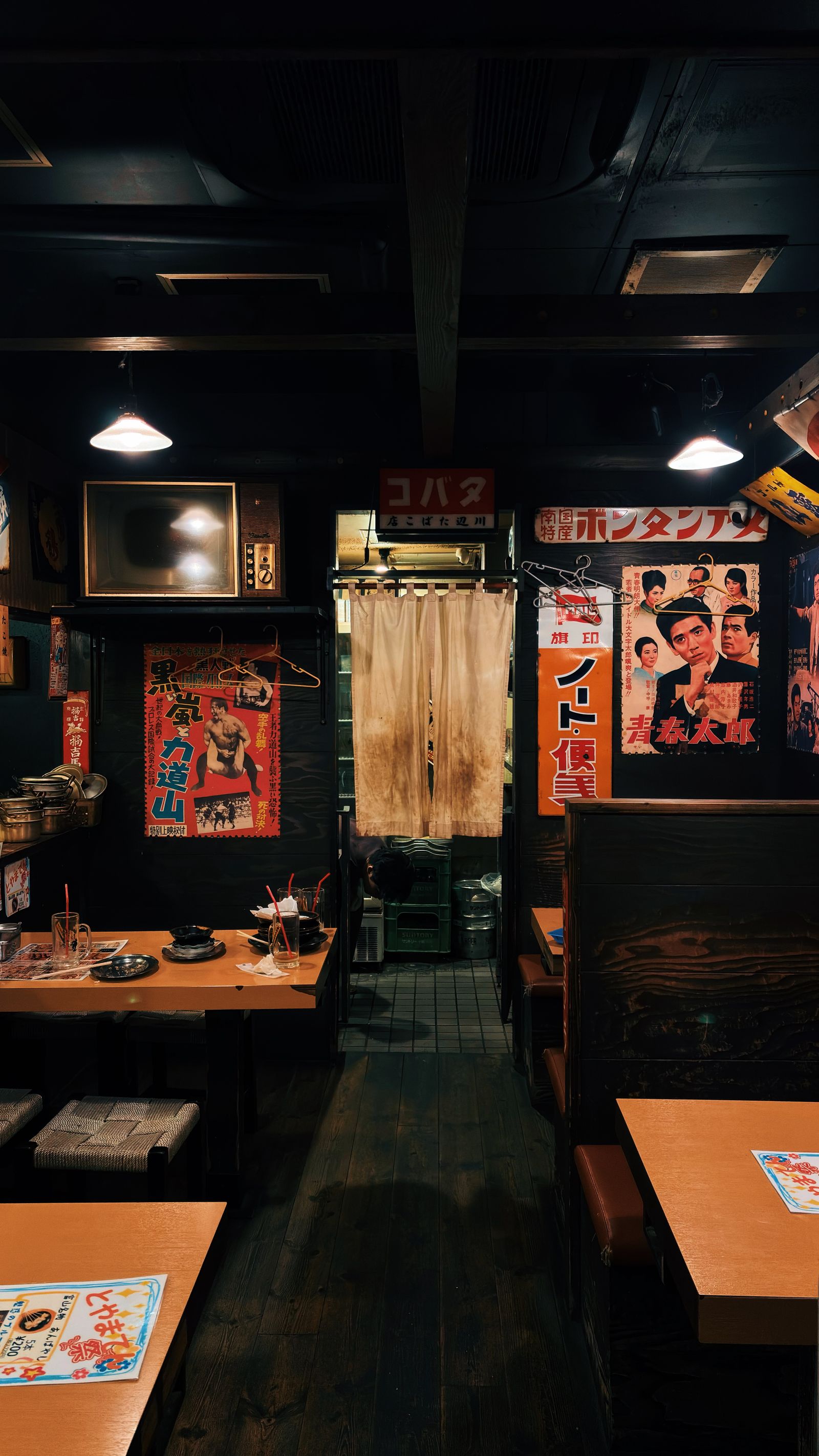 暖簾と昭和のポスターが残る、木のテーブルの飲食店の店内